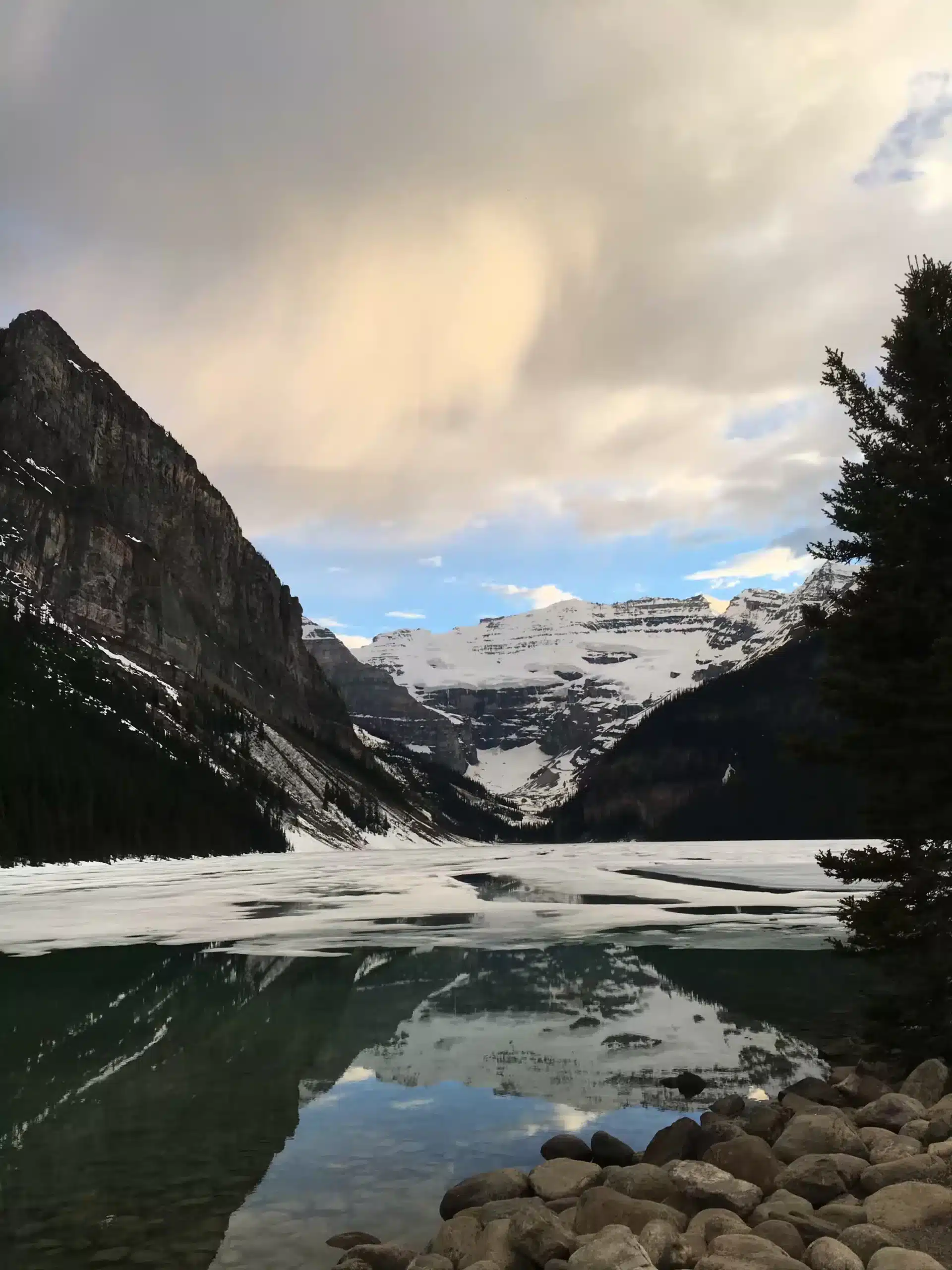 A partially frozen alpine lake and snow-capped peaks on a Vancouver to Banff road trip